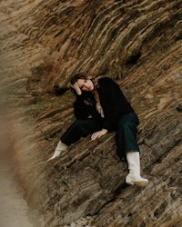 a woman sitting on a rock in front of a body of water